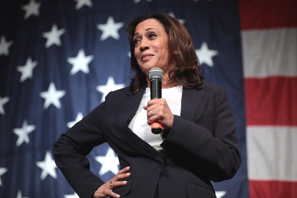 Kamala Harris speaking into a microphone in front of an American flag.